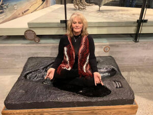Deb Hall in a meditative pose inside a fossilized dino footprint at a museum